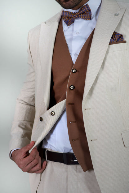 Елегантен мъжки костюм от три части в светлобежов цвят с вталена slim fit кройка, кафява жилетка и папийонка, подходящ за сватба или бал.